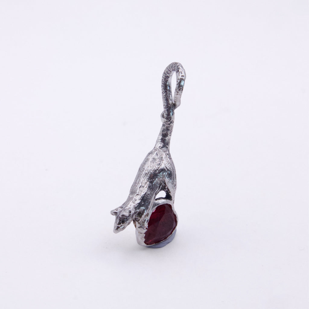 A silver pendant shaped like a leaping rat holding a dark red gemstone, shown on a plain white background.