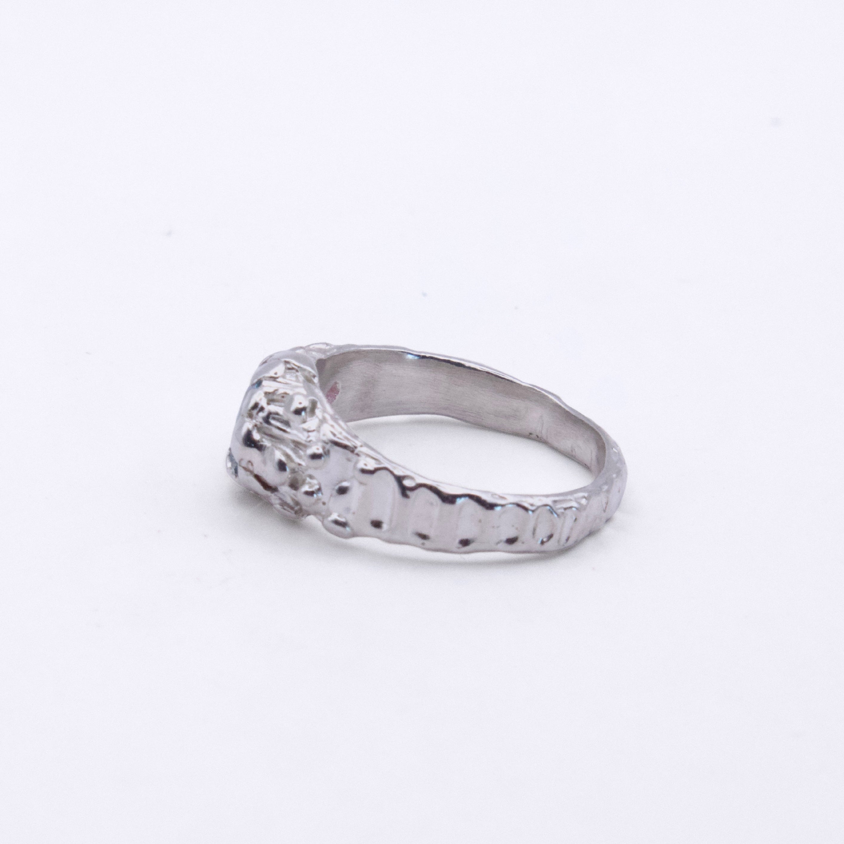 A silver ring with a textured, hammered band and a decorative, raised top section, photographed on a plain white background.