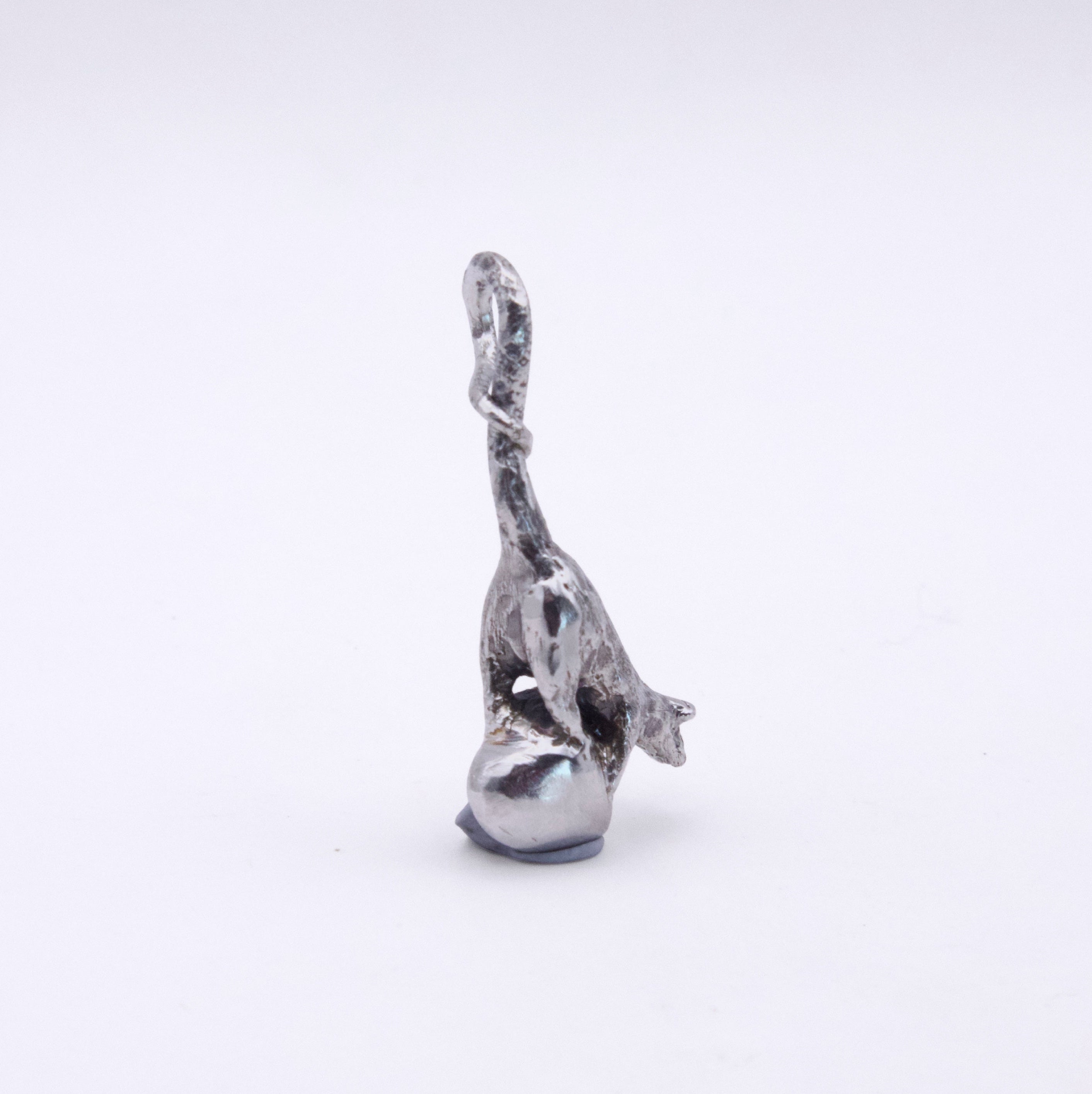 A small silver-toned metal figurine of a stylized rat standing on a heart shaped base, photographed against a plain light gray background.
