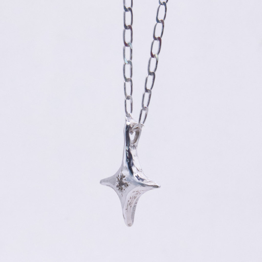 A silver pendant necklace featuring a textured, four-pointed star or compass-like charm hanging from a delicate silver link chain, set against a plain white background.