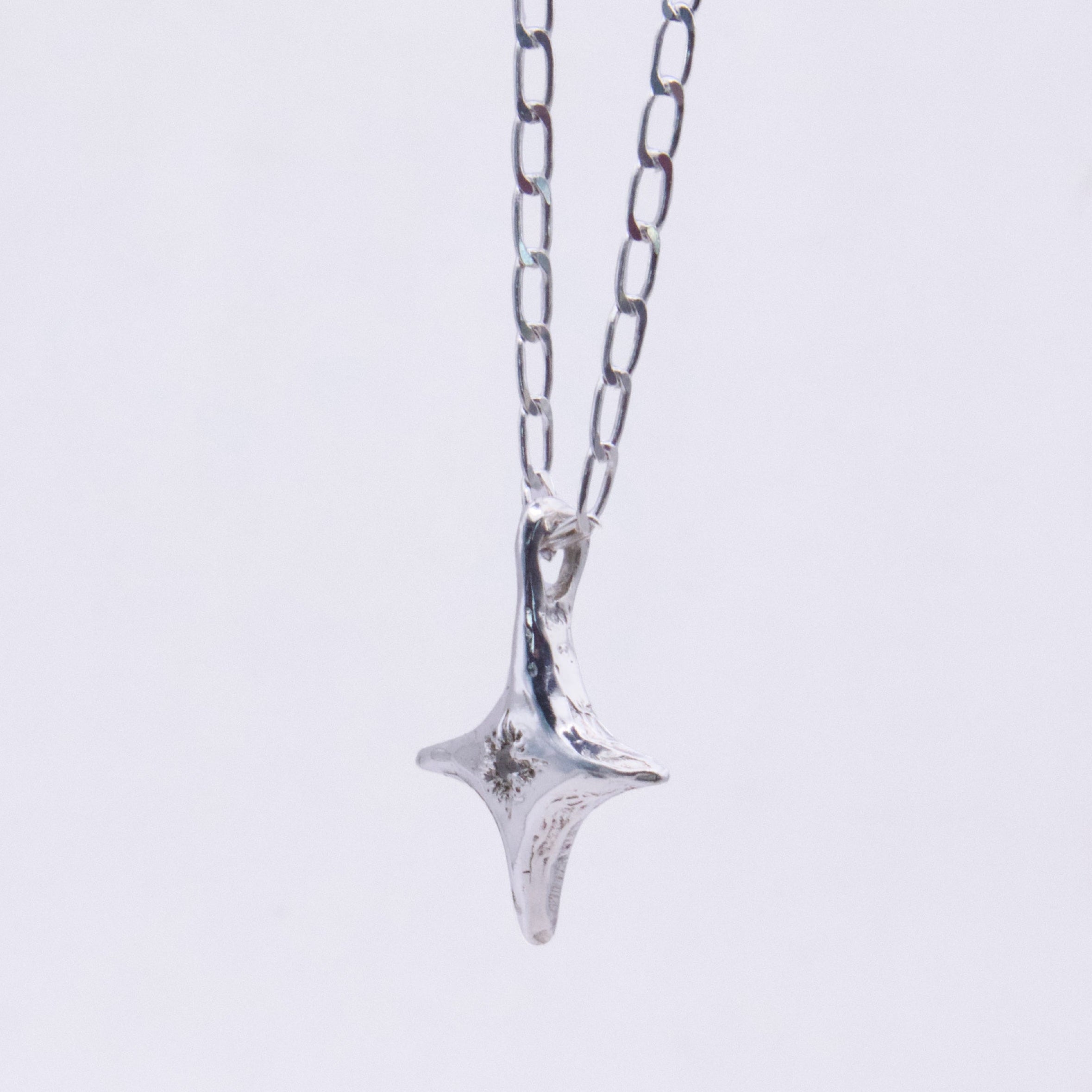 A silver pendant necklace featuring a textured, four-pointed star or compass-like charm hanging from a delicate silver link chain, set against a plain white background.