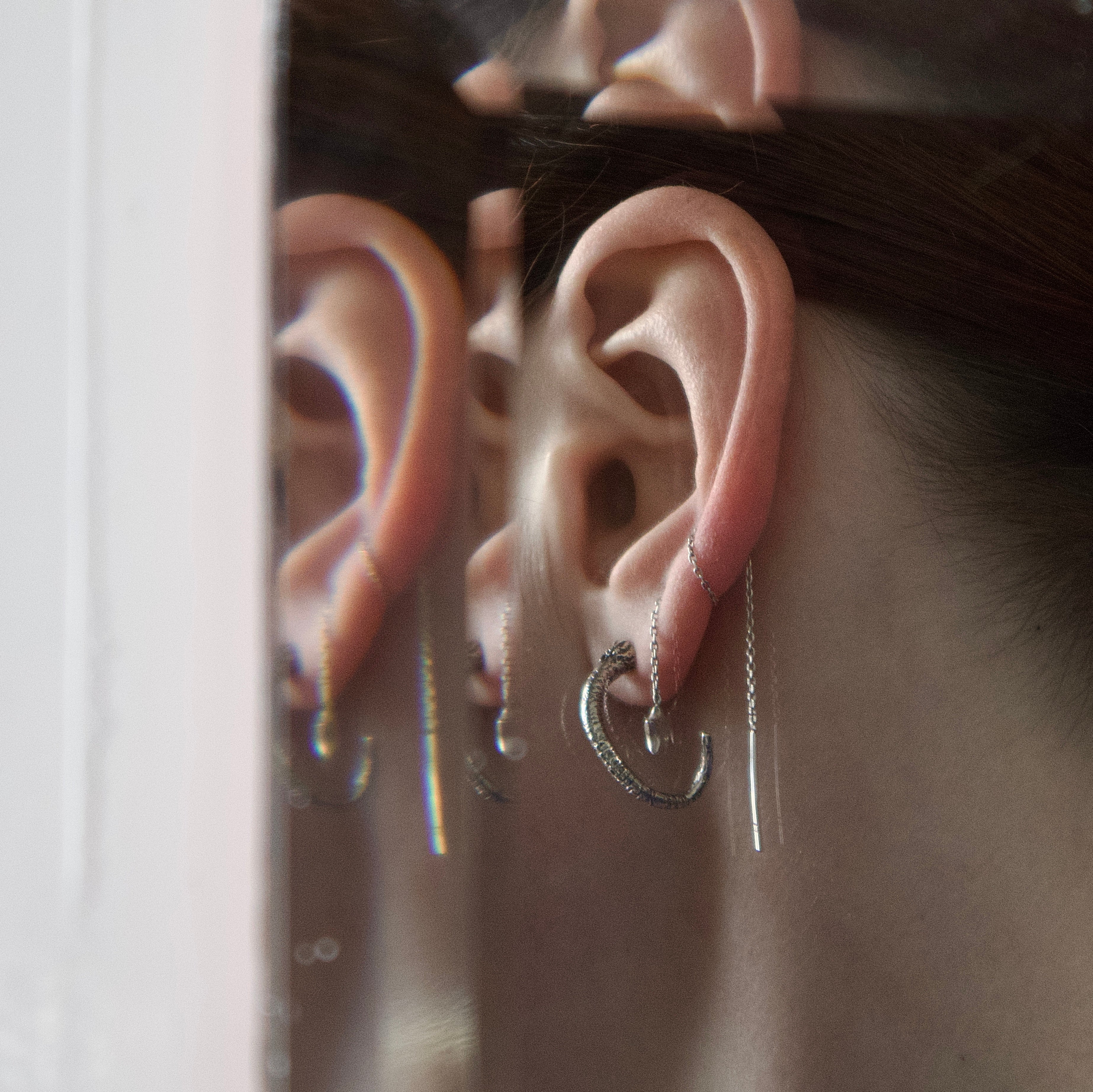 Close-up of an ear with sterling silver rat tail earrings against a mirrored background