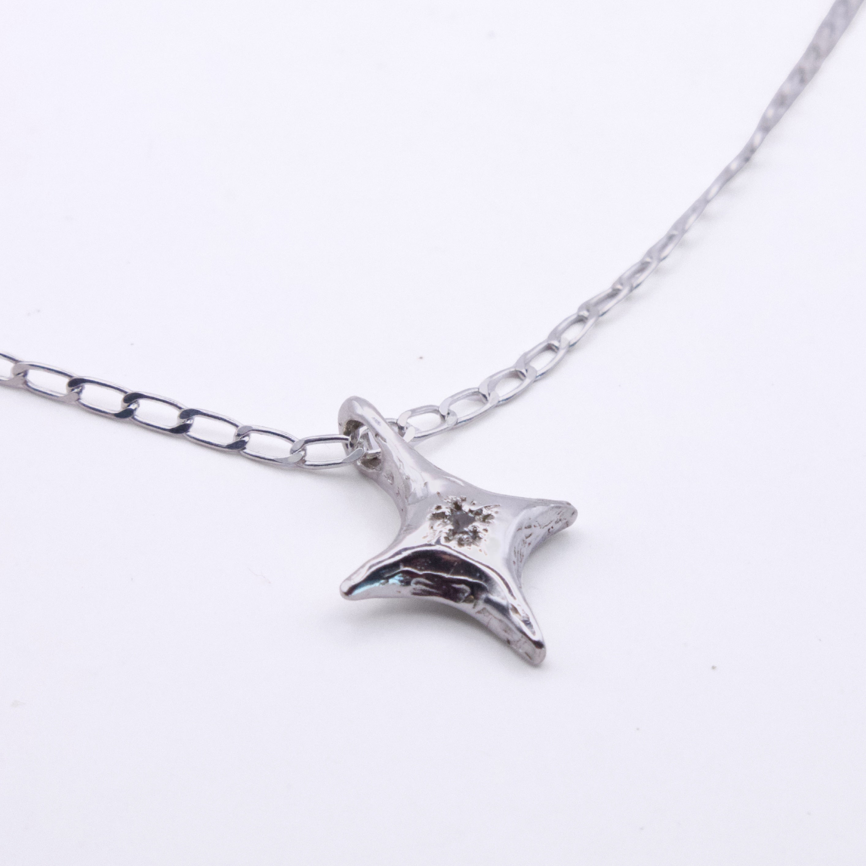 A silver-toned starfish pendant necklace on a matching link chain, featuring a small clear crystal detail on the starfish, set against a plain white background.