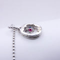 A silver Y2K pendant necklace with a small central pink gemstone and a blue accent stone, shown on a plain light gray background.
