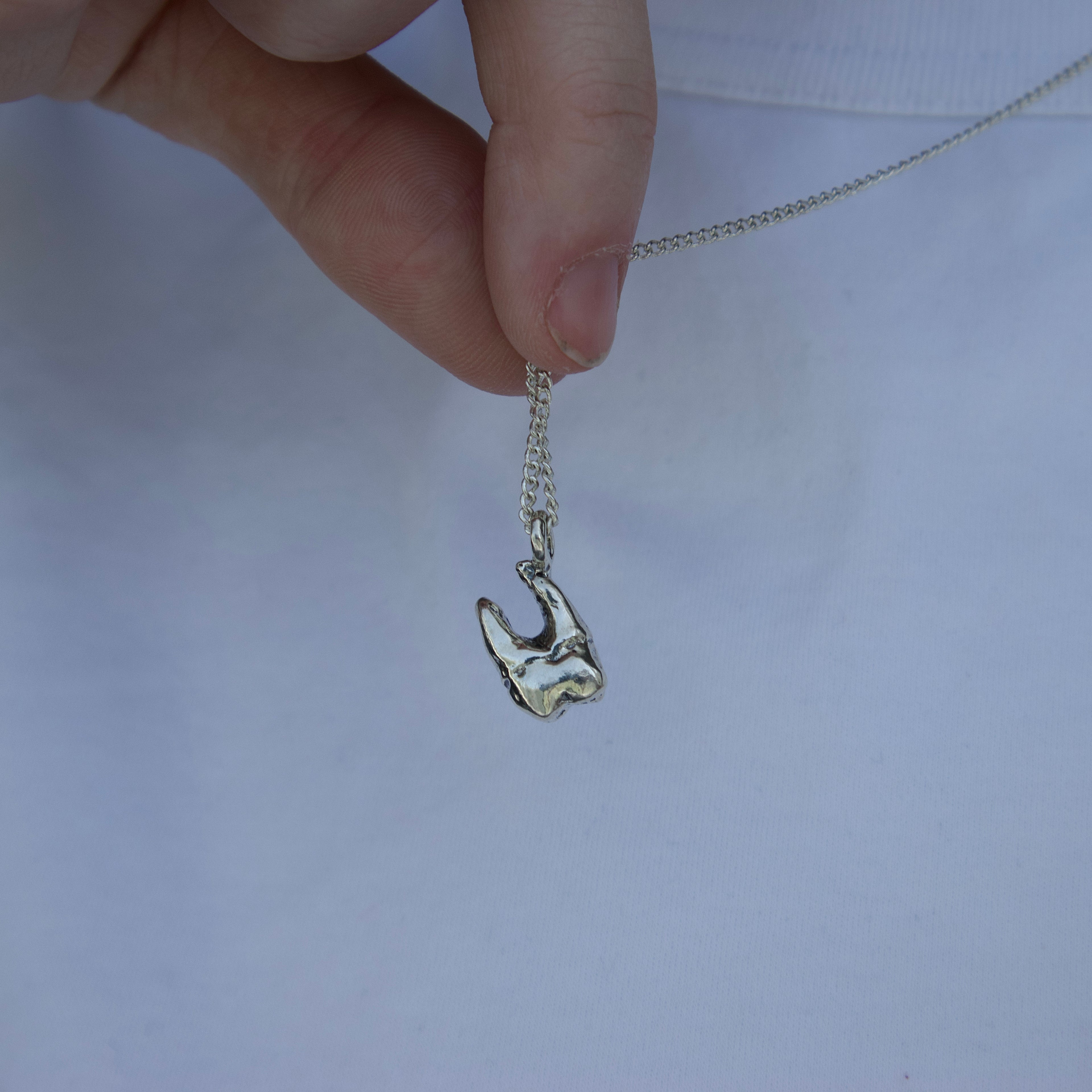 Hand holding a silver necklace with a unique pendant  of a sterling silver tooth with roots against a plain background